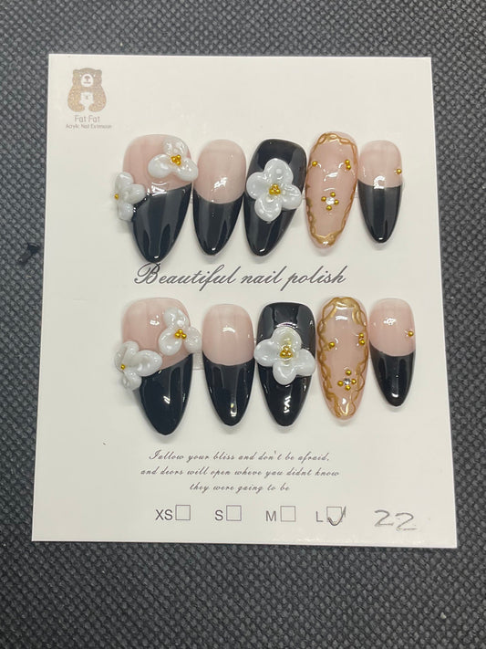 Nude and black coffin press-on nails featuring 3D white flowers and gold gems. 