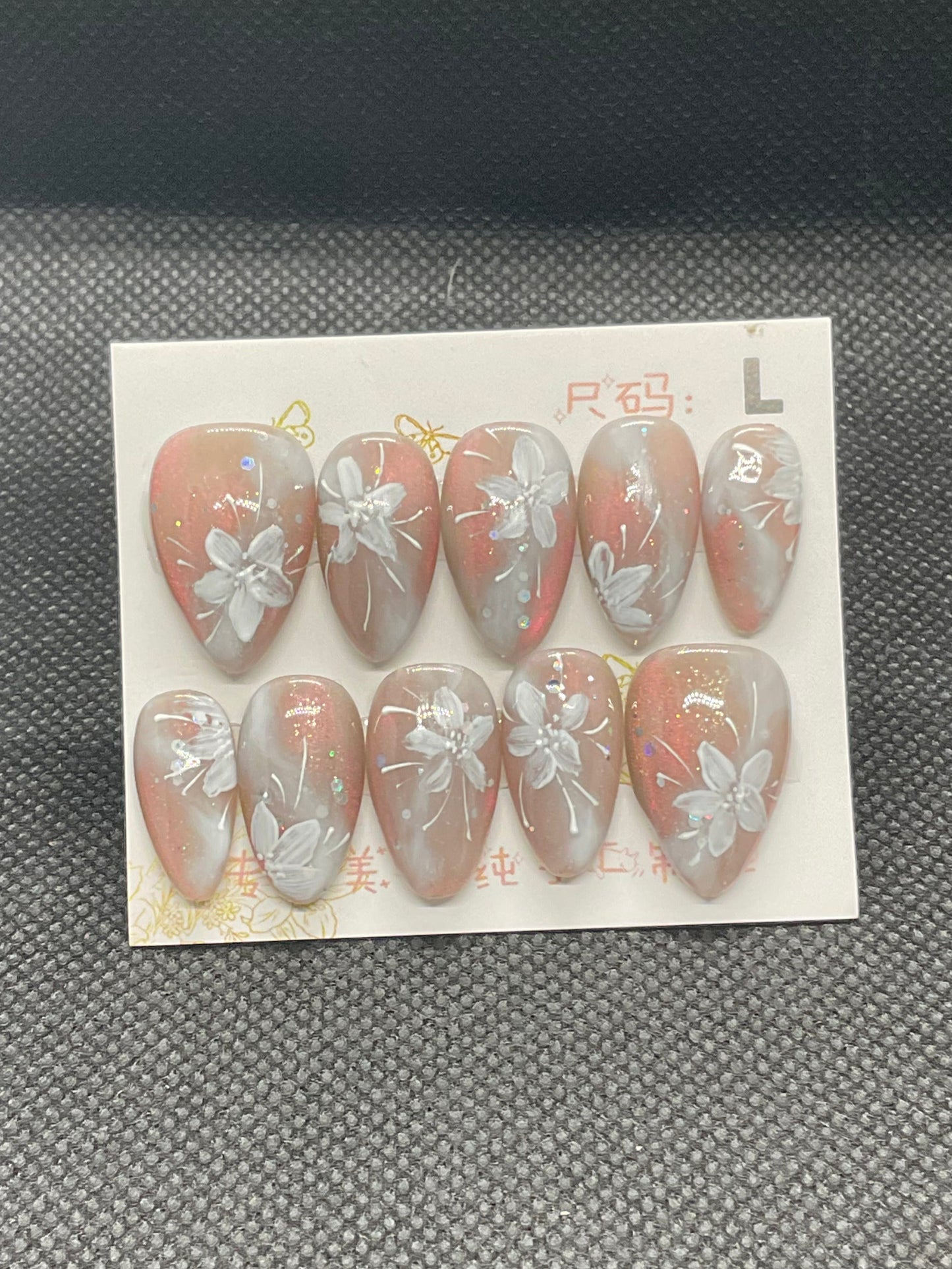 Coral ombre almond nails with soft shimmer and white floral accents.