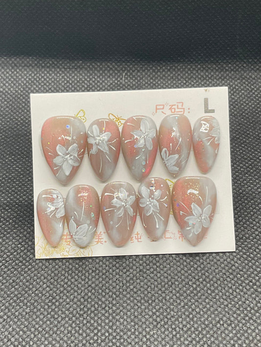 Coral ombre almond nails with soft shimmer and white floral accents.